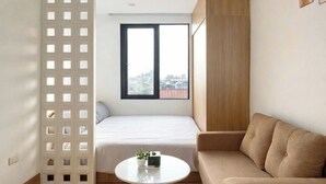 Un espacio habitable moderno y funcional con cama, sofá, una mesita y vistas a la ciudad por una ventana.