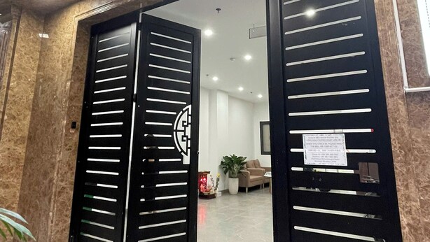Entrada de un hotel con dos portones negros, suelo de mármol y una recepción visible en el interior.