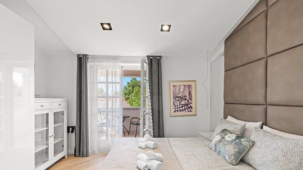 Ein modernes Schlafzimmer mit einem großen Bett, einem Kleiderschrank und einem Balkon mit Sitzgelegenheit.