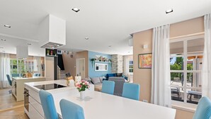Eine moderne Küche mit einer zentralen Kochinsel, einem Essbereich mit blauen Stühlen und einem Wohnbereich mit Sofa und Kamin.