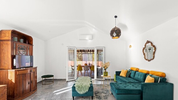 Un salon spacieux avec un canapé de couleur turquoise, un meuble en bois et une vue sur une terrasse extérieure.