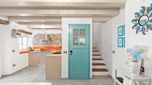 Eine moderne Küche mit einer Rückwand aus Stein, einer türkisblauen Tür und einer Treppe, die in ein weiteres Geschoss führt.