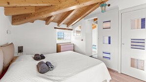 Ein Schlafzimmer mit Holzboden, einem Bett mit weißer Bettdecke, zwei gerollten Handtüchern, einem Nachttisch und einem Fenster mit Blick.