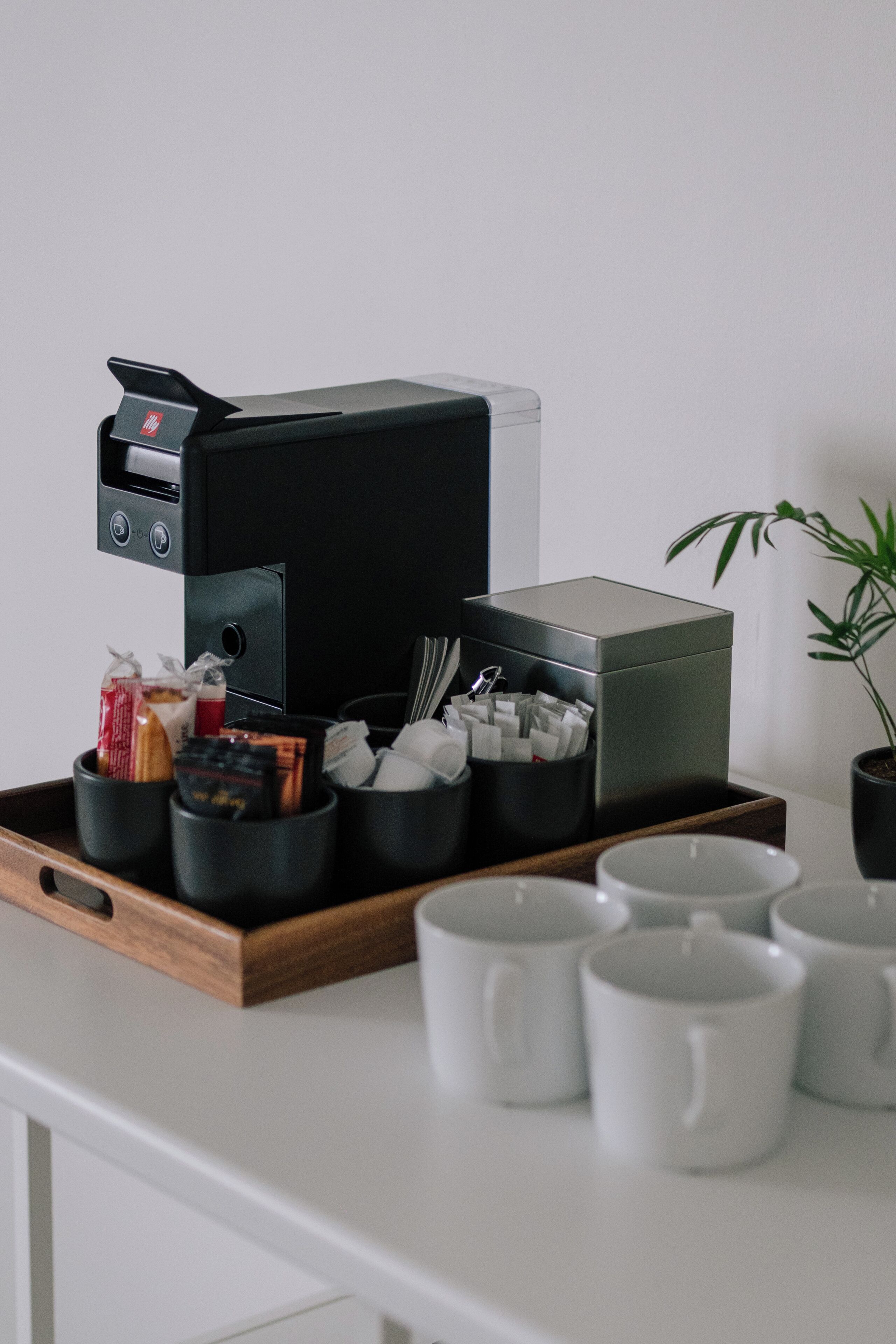 A coffee machine on a tray with cups and a plant.