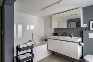 Een moderne badkamer met een badkuip, een wastafel met spiegel en een toilet.