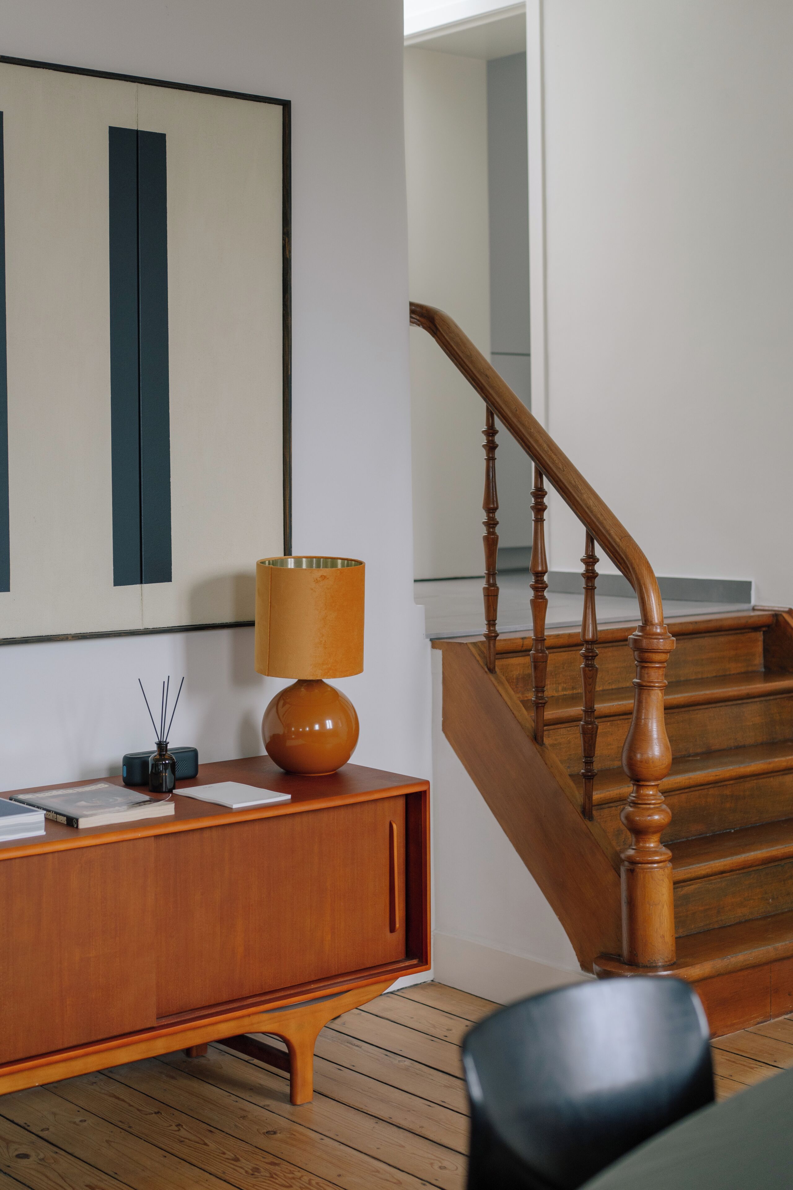 Una escalera de madera con diseño curvo, una consola de madera con una lámpara, y una obra enmarcada en la pared.