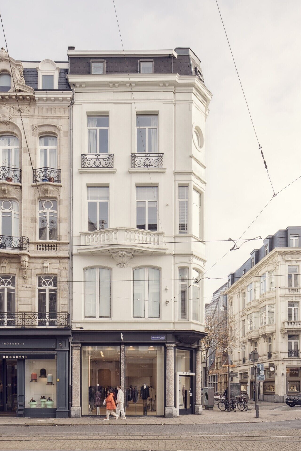 A corner building with a shop on the ground floor, large windows, and a tram line overhead.