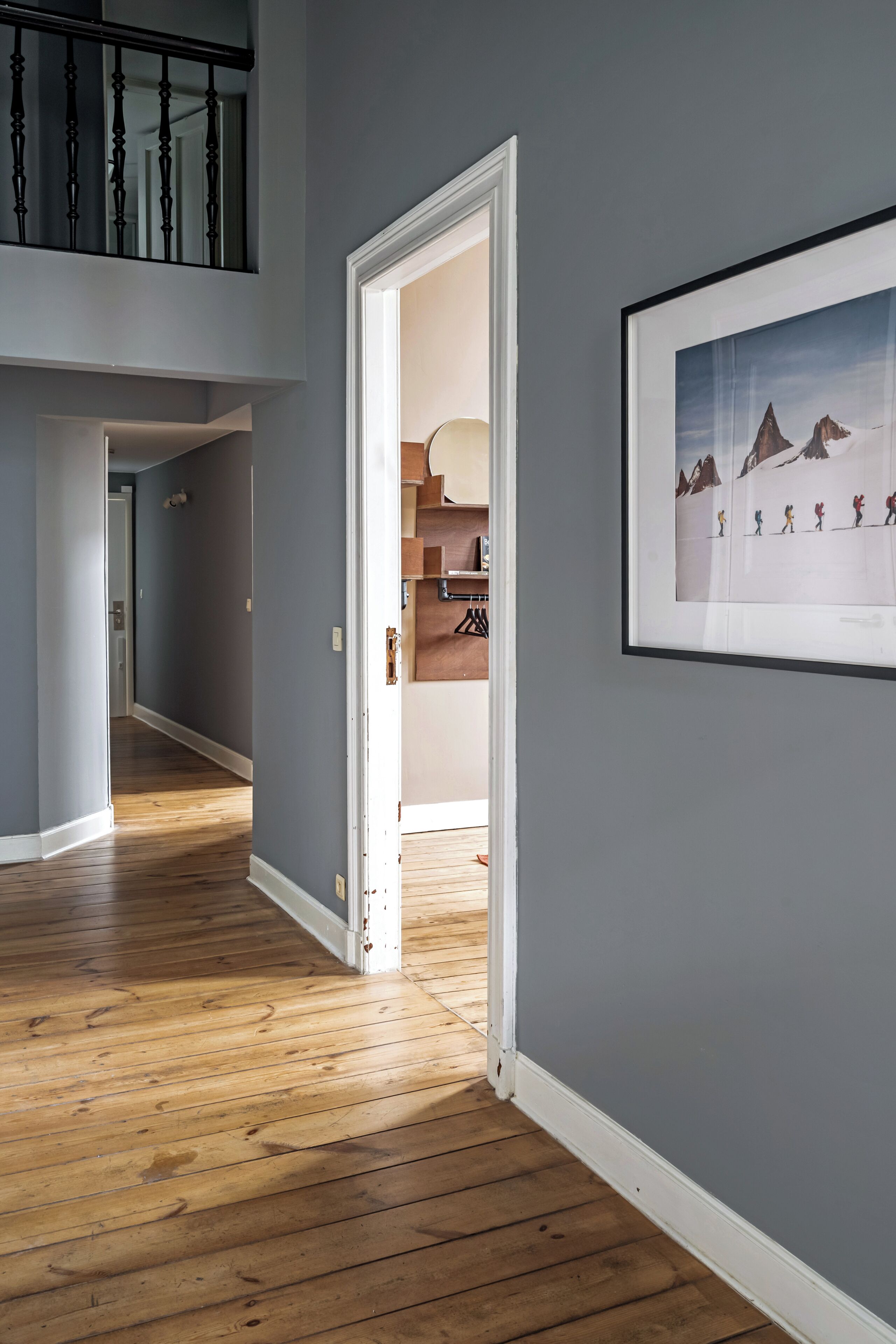A hallway with wooden flooring, a white door, and a framed picture on the wall.