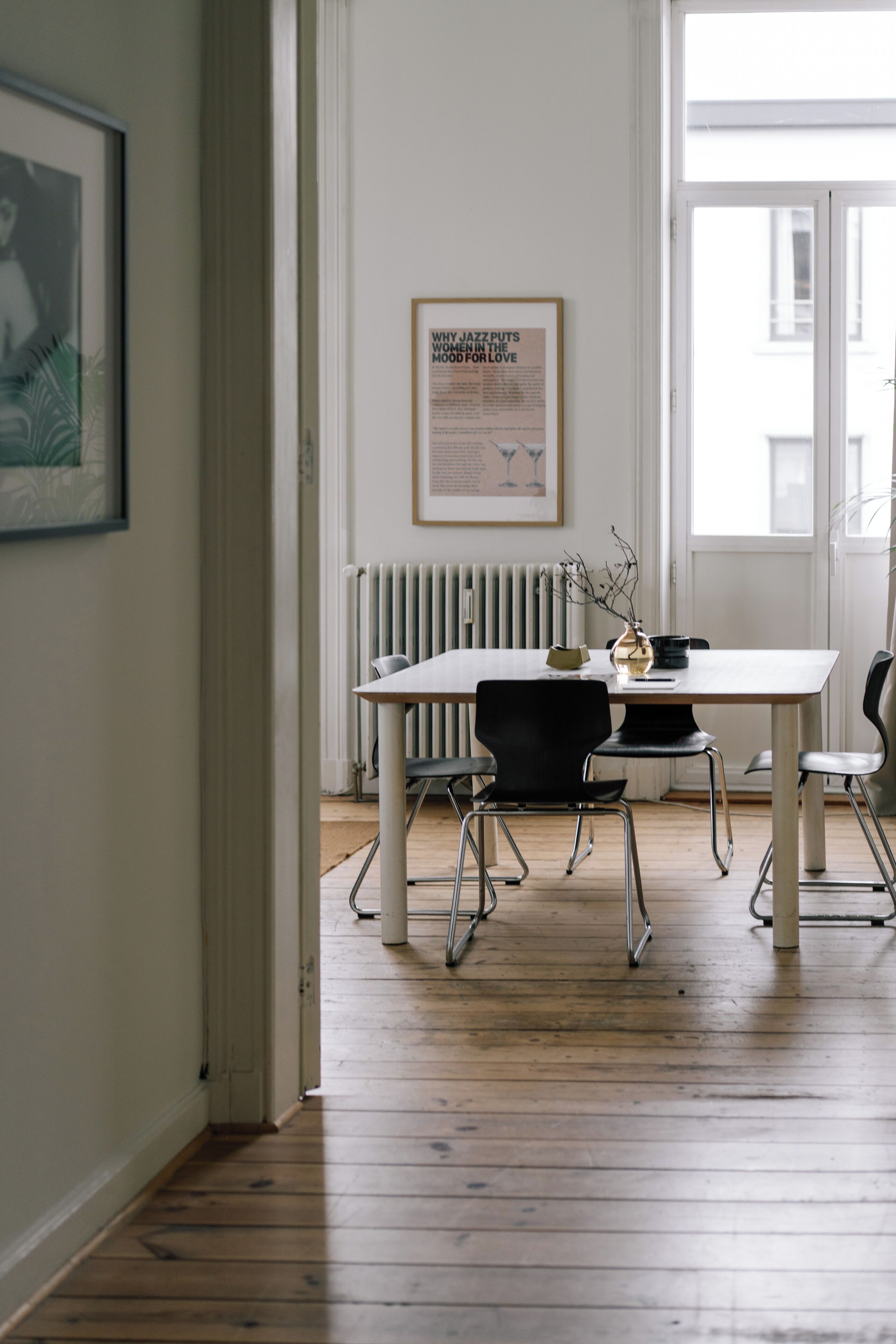 A room with a white table, black chairs, a framed poster on the wall, and a radiator.