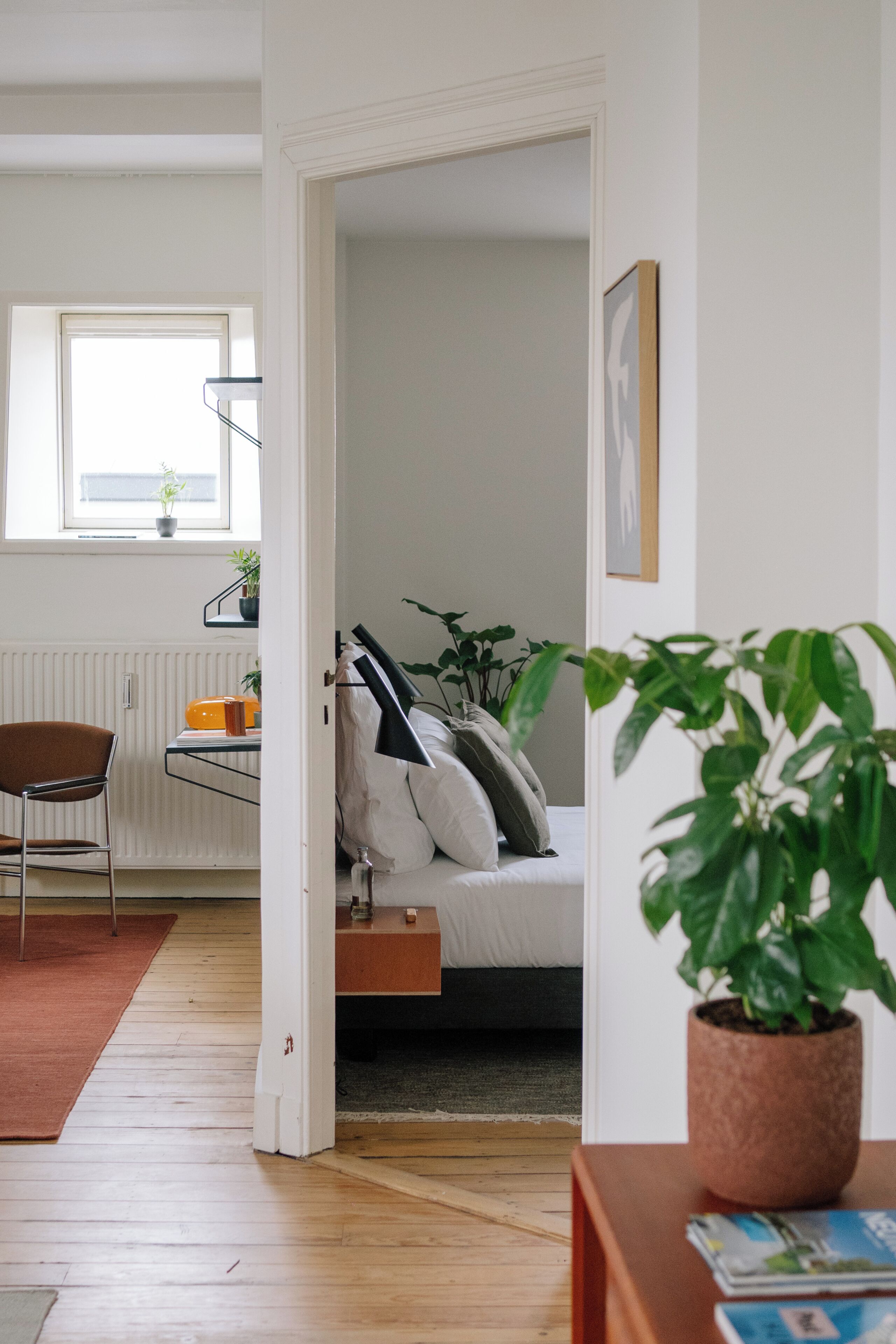 Een kamer met een bed, een stoel, een radiator, een raam en een potplant.