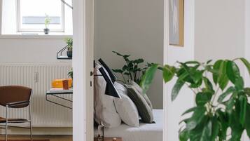 Een kamer met een bed, een stoel, een radiator, een raam en een potplant.