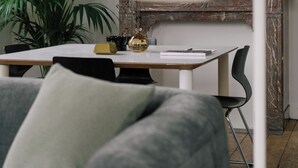 Un salon moderne avec un canapé gris, un bureau blanc, un miroir rond et une plante en pot.