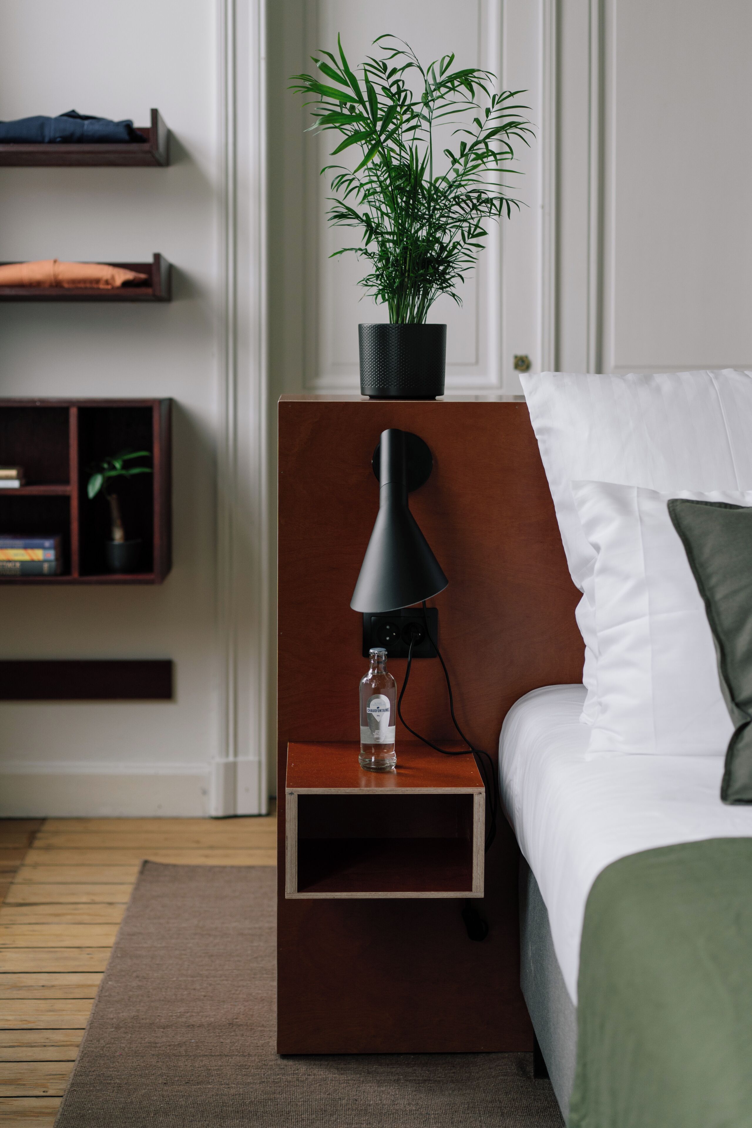 A neatly arranged bedroom with a bed, bedside table, lamp, and a potted plant.