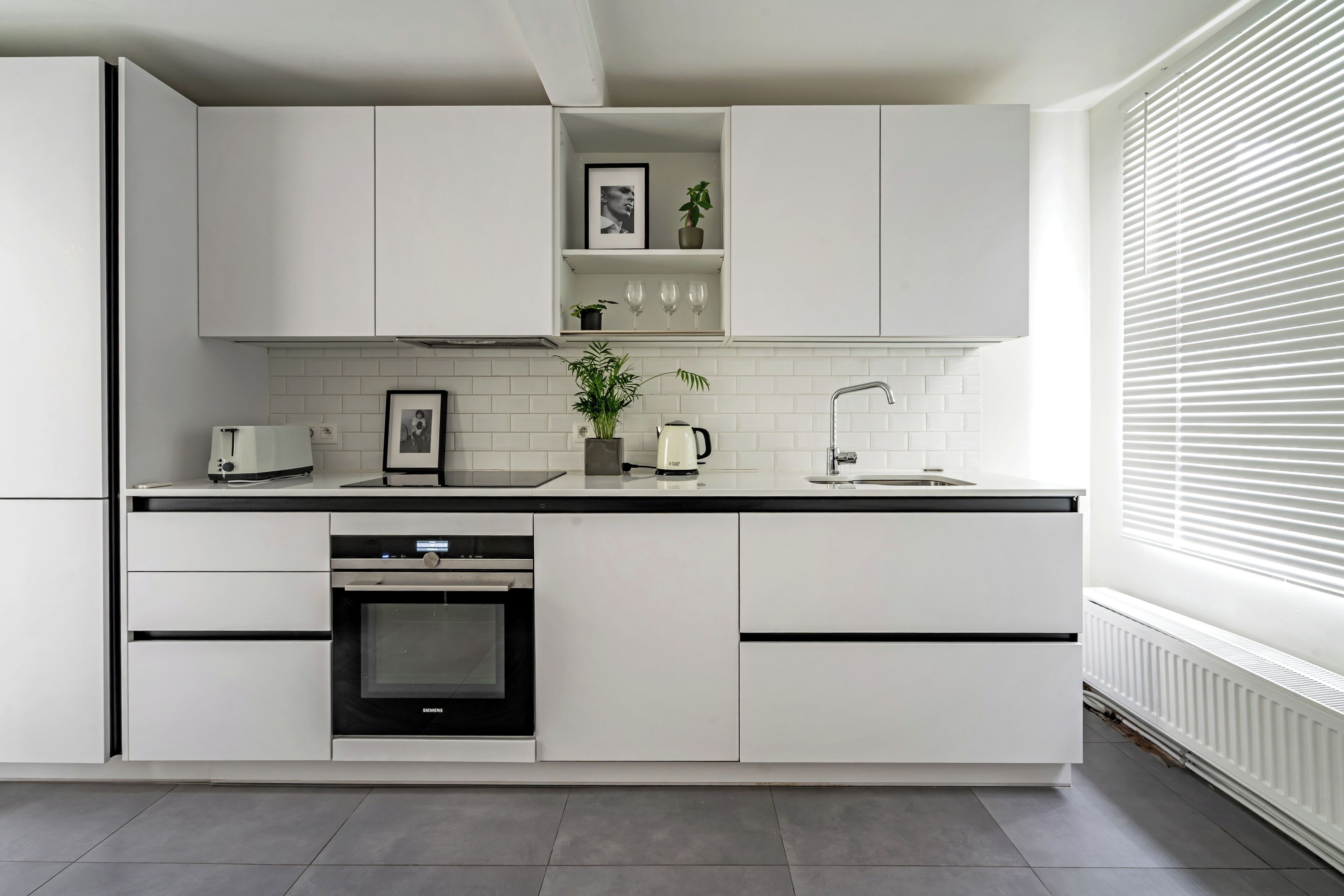 A modern kitchen with white cabinets, a built-in oven, a coffee maker, and a sink.