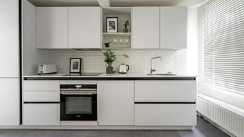 A modern kitchen with white cabinets, a built-in oven, a coffee maker, and a sink.
