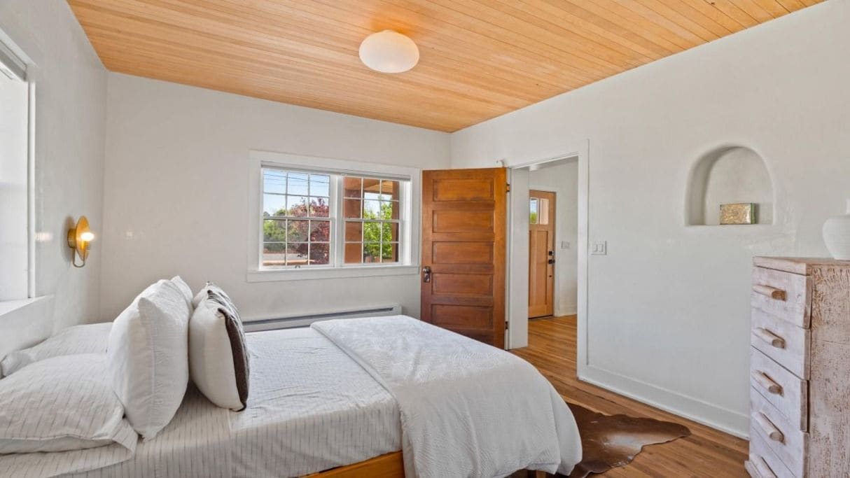 Un dormitorio con cama, ventana, puerta y cómoda.