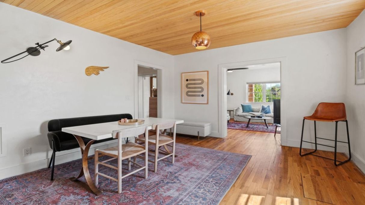 A modern interior with a dining area, a sofa, a bar stool, and a patterned rug.