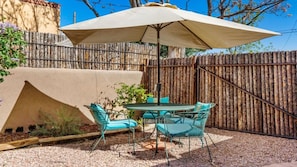 An outdoor patio with a round table and chairs, a large umbrella, and a wooden fence. - 2-bedroom house in lovely Santa Fe (Santa Fe)