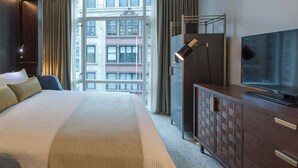 Et hotelværelse med en stor seng, fjernsyn, kommode og et vindue med udsigt over byen.