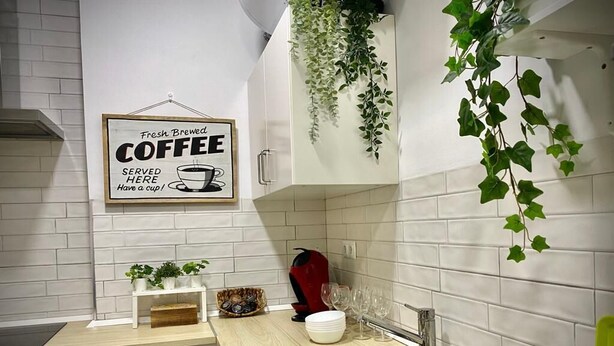 Een keuken met een roestvrijstalen spoelbak, een koffieapparaat en een bordje met de tekst 'Verse koffie wordt hier geschonken. Geniet van een kopje!'