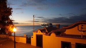 A coastal building with a tiled roof, a street lamp, and a view of the sea and a cruise ship in the distance. - VCGuesthouse Grandfather's Room (Funchal)