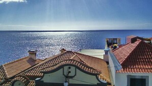 A coastal view with a clear sky, a calm sea, and buildings with red-tiled roofs. - VCGuesthouse Grandfather's Room (Funchal)