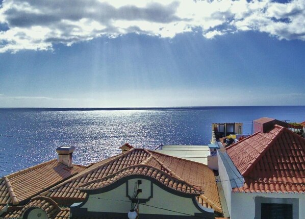 A coastal view with a clear sky, a calm sea, and buildings with red-tiled roofs. - VCGuesthouse Grandfather's Room (Funchal)