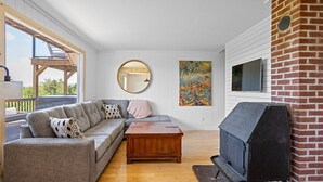 Uma sala de estar moderna com sofá seccional, mesa de centro de madeira, espelho redondo, pintura abstrata colorida e lareira de tijolos.