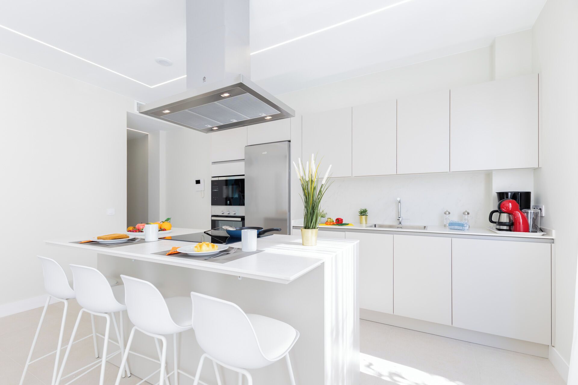 A modern kitchen with white cabinetry, a central island with bar stools, a built-in oven, and a coffee machine.