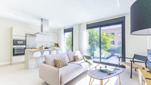 En moderne lejlighed med et køkken, en opholdsstue med sofa og sofabord, samt store vinduer med udsigt.