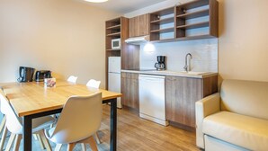 Een kleine keuken met een houten tafel, stoelen, een koffiezetapparaat, een magnetron en een vaatwasser.