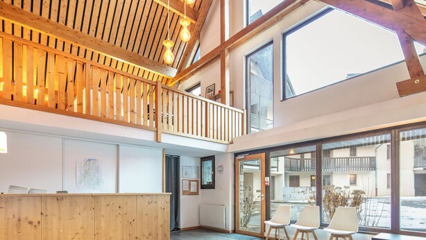 Een ruime lobby met een houten receptiebalie, een balkon met houten hekwerk en grote ramen met uitzicht op buiten.