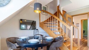A dining area with a round table, grey upholstered chairs, and a wooden staircase. - Ferienwohnung mit Balkon in St.Peter-Ording (St Peter-Ording)