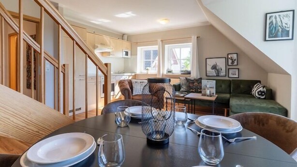 A dining area with a round table, chairs, and a decorative centerpiece. A staircase leads to a kitchen area with a microwave and cabinets. - Ferienwohnung mit Balkon in St.Peter-Ording (St Peter-Ording)