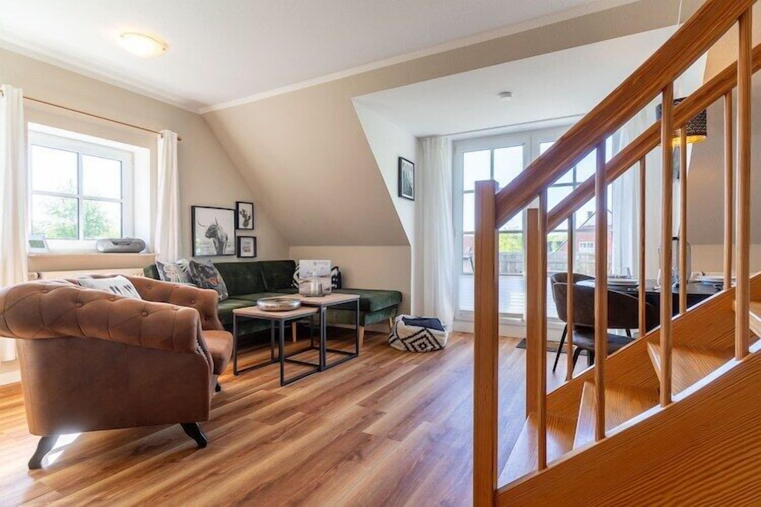 Un salon spacieux avec un canapé en cuir marron, un divan vert et un escalier en bois.