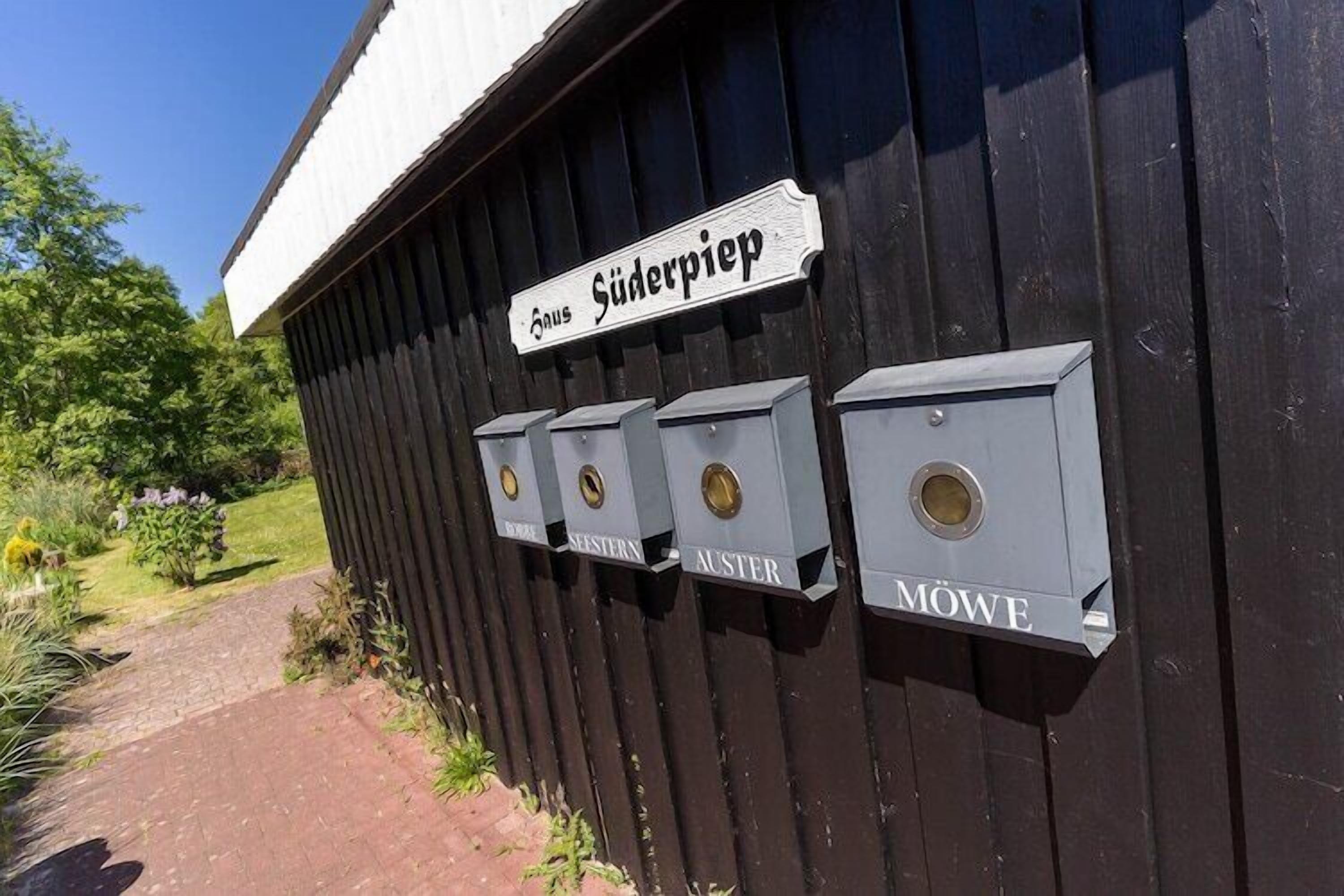 A black wooden building with a sign reading "Süderpiep" and mailboxes labeled "BOSSE," "SEESTERN," "AUSTER," and "MOWE."
