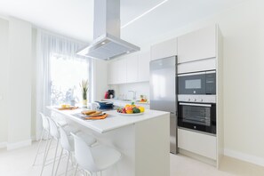 Eine moderne Küche mit weißen Schränken, einer zentralen Kochinsel mit Sitzgelegenheit, einem eingebauten Backofen und einer Mikrowelle.