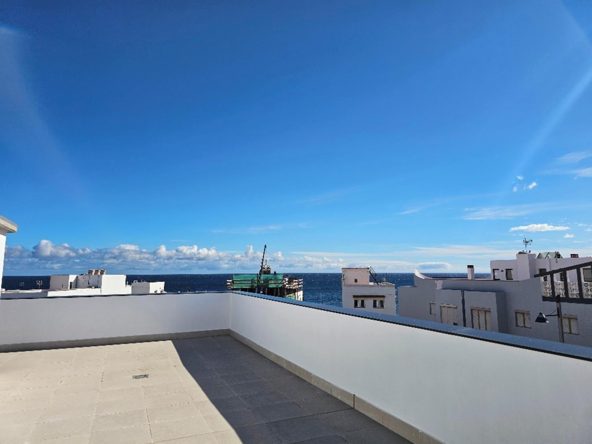 Una terraza en la azotea con vistas despejadas al mar y edificios lejanos.