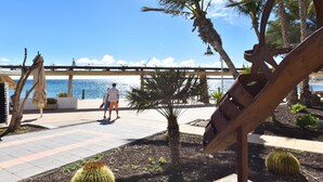 A coastal walkway with palm trees, a cactus, and a metal sculpture. - Suites Brisamar V by VillaGranCanaria (Las Palmas de Gran Canaria)