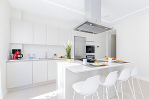 Eine moderne Küche mit weißen Schränken, einer zentralen Kochinsel mit Barhocker, einer Kaffeemaschine und einem Kühlschrank.
