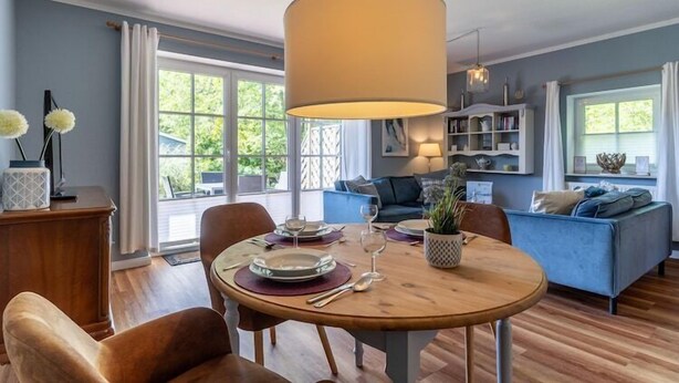 Een eetgedeelte met een ronde tafel, stoelen en een hanglamp. Achtergrond toont een bank en een boekenkast.