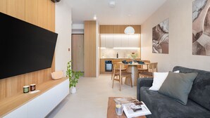 Een moderne woonkamer met een flatscreen televisie, een bank, een salontafel en een eethoek met een tafel en stoelen.