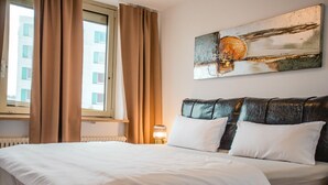A hotel room with a bed, curtains, a window, a wall-mounted painting, and a bedside lamp. - AMA Executive Stay 65m² Near Central Station (Nuremberg)
