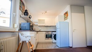 A compact kitchen with a microwave, oven, washing machine, and a small dining table. - AMA Executive Stay 65m² Near Central Station (Nuremberg)