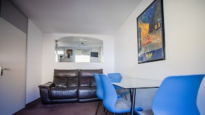 A room with a brown leather sofa, blue chairs, a glass table, and a painting on the wall. - AMA Executive Stay 65m² Near Central Station (Nuremberg)