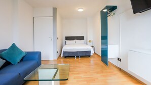 Ein modernes Hotelzimmer mit einem Bett, einem blauen Sofa, einem Glastisch und einem Kleiderschrank.