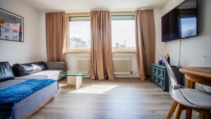 A modern living room with a sofa, a glass coffee table, a TV, and a dining area with a table and chairs. - AMA Executive Stay 65m² Near Central Station (Nuremberg)