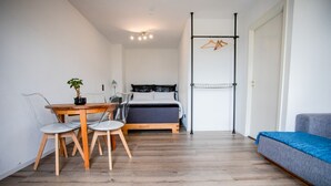 A compact room with a bed, a sofa, a dining table with chairs, and a hanging clothes rack. - AMA Executive Stay 65m² Near Central Station (Nuremberg)