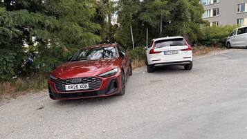 Ein rotes Auto steht auf einem Schotterweg, dahinter ein weißes Auto.