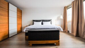 A modern bedroom with a bed, a nightstand, a lamp, and a view of the outdoors through large windows. - AMA Executive Stay 65m² Near Central Station (Nuremberg)